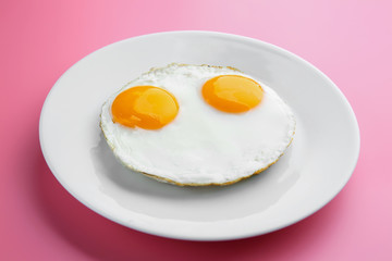 Plate with delicious sunny side up eggs on colour background