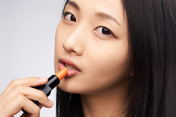 Obraz premium Beautiful young woman on a light background paints lips, asian