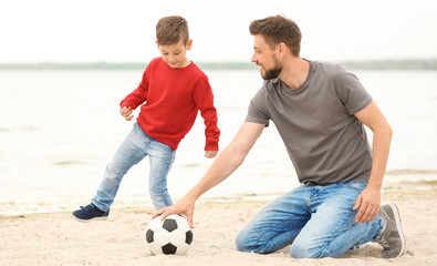 Dad and son playing football together on the beach