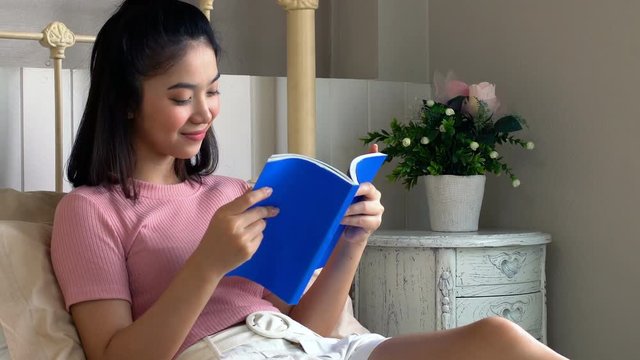 Asian young female reading book on mattress in bedroom