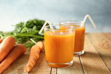 Two glasses of homemade carrot juice with vegetables on wooden table