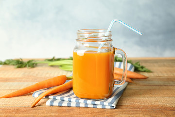 Mason jar of fresh carrot juice with vegetables on wooden table