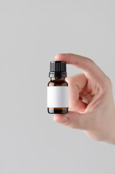 Dropper Bottle Mock-Up. Blank Label - Male hands holding a dropper bottle on a gray background