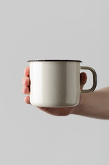 White Enamel Mug Mock-Up - Male hands holding an enamel mug on a gray background