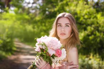 Fototapeta premium Beautiful young woman with bouquet of peonies in spring park on sunny day