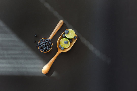 Fresh juicy blueberry fruits with limes on a wooden spoon against a dark background