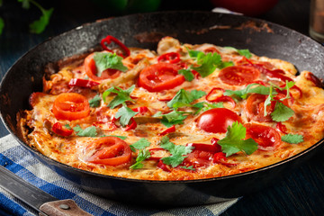 Frittata made of eggs, sausage chorizo, red pepper, green pepper, tomatoes, cheese and chili in a pan on wooden table
