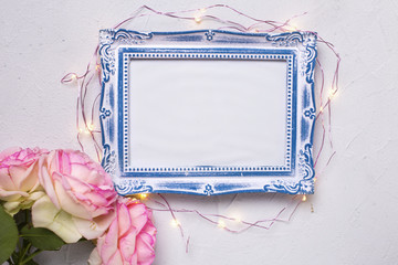 Empty photo frame, flowers  and fairy lights on grey textured background. Top view. Flat lay. Place for text. Mock up.