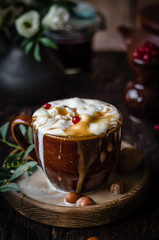 iced coffee with ice cream and caramel in a brown cup on a wooden plate with nuts, red currant in a pot on a brown wooden table