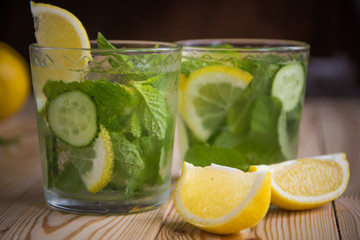 Detox water, fresh organic lemonade with ice, cucumber, lemon and mint on wooden background