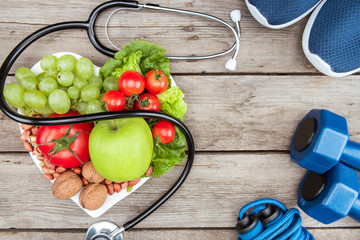 top view of stethoscope, organic vegetables and fruits and sport equipment on wooden surface, healthy lifestyle concept