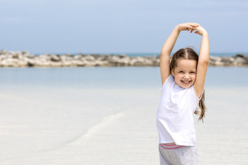 Happy child on the beach. Paradise holiday concept, girl seating on sandy beach with blue shallow water and clean sky