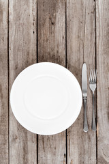 top view of arranged empty plate, fork and knife on wooden table
