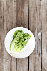 top view of fresh letuce salad on plate with cutlery on wooden table, healthy eating concept