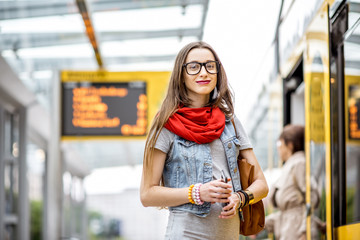 Portrait of a young woman waiting for the public transport standing on the tram stop with timetable...
