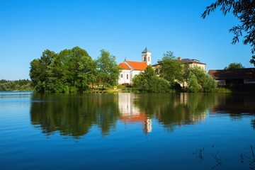 Fototapeta na wymiar Village church with tree on shore of pond, Czech republic, Blato.