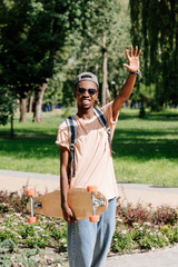 stylish african american man with outstretched arm holding longboard