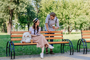 smiling multicultural couple having conversation while sitting on bench in park