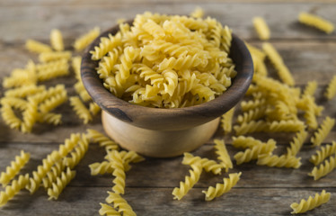 Pasta fusilli in a wooden bowl on wood background for healthy recipes.