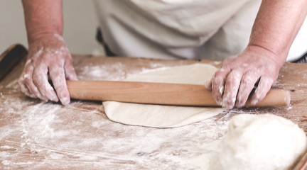 Grand mother makes round shape from pastry using rolling pin