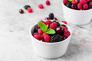 Summer fresh berries in white bowl on gray concrete table background. Copy space. Vegetarian food - raspberry, blackberry and cherry