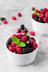 Summer fresh berries in white bowl on gray concrete table background. Copy space. Vegetarian food - raspberry, blackberry and cherry