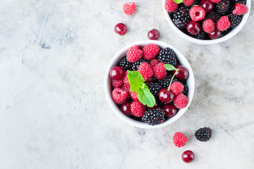 Summer fresh berries in white bowl on gray concrete table background. Top view with copy space. Vegetarian food - raspberry, blackberry and cherry