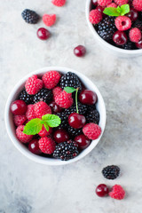 Summer fresh berries in white bowl on gray concrete table background. Top view with copy space. Vegetarian food - raspberry, blackberry and cherry