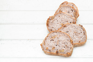 Slices of walnut bread on white wooden background
