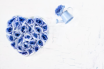 Artificial blue roses in the shape of heart on a white cracked background. Lots of free space.
