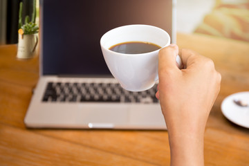 Hand holding a coffee cup with laptop sitting on the table