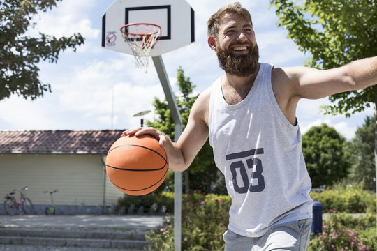 Laughing man playing basketball on outdoor court