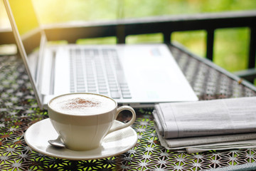 Stock photo :.Cappuccino with newspaper ,laptop or notebook. on vintage table in morning activity concept on nature sunlight background