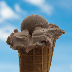 Scoop of ice in cone, close up against blue sky with clouds