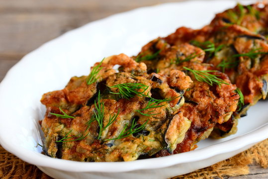 Fried eggplant cutlets. Crispy eggplant cutlets with garlic and dill on a white plate and a vintage wooden table. Easy vegetarian eggplant recipe. Closeup