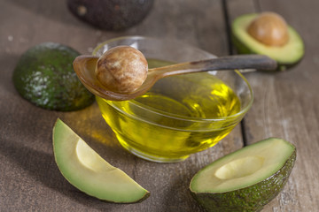 Fresh whole and sliced avocado and a cup of oil ongreen craked wooden table- cooking, spa, bodycare concept