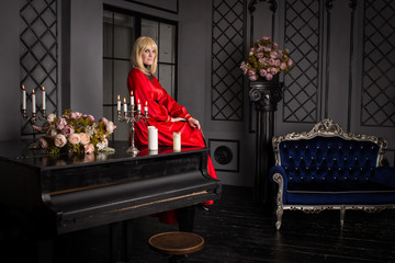 Beautiful blond woman sitting on the couch. She is dressed in a luxurious, expensive, red dress.