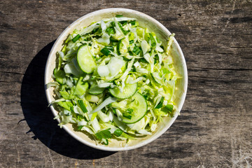 Spring vegan salad with cabbage, cucumber, green onion and parsley on wooden table
