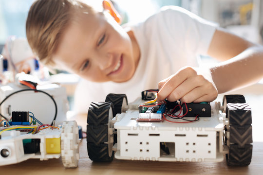 Fair-haired boy adjusting wires in robotic car