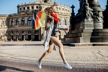 Lifestyle portrait of a young woman tourist jumping with german flag in front of the Opera house in Dresden city, Germany