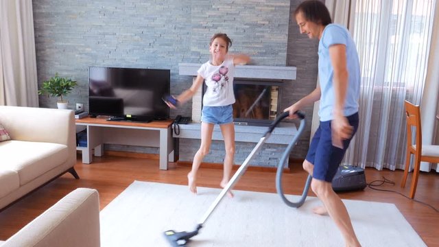 A happy family. Dad and daughter having fun in a clean house. A man is dancing with a vacuum cleaner.