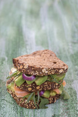 Countrybread Avocado, salted salmon sandwich with fresh herss on green craked paint wooden board background. Healthy eating theme