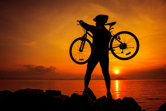 Healthy lifestyle. Silhouette of bicyclist carrying his bicycle on shoulder. Outdoors.
