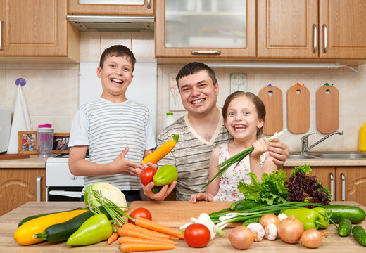 Father and two children in home kitchen interior. Happy family, girl and boy having fun with fruits and vegetables. Healthy food concept.