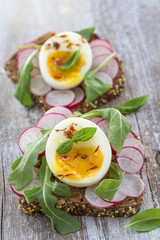 A hearty whole wheat sandwich with arugula, radishes and eggs on wooden background