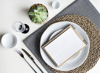 Table setting. White dishware, monochrome napkins, Cutlery, glass and plants.