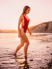 Fototapeta na wymiar Pretty beautiful woman in red swimwear on ocean with warm sunset colors