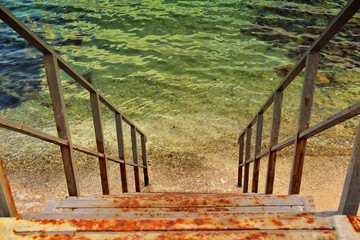 Rusty iron stairs descending into sea. Horizontal orientation