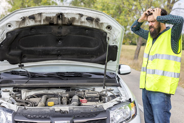 Worried young man examining his car engine parked on the side of a road