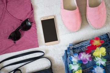 perfect summer festival outfit accessories. flat lay of a trendy woman fashion outfit. denim jeans, pink top shirt, espadrilles, sunglasses, black purse and a elegant smartphone. top view.


